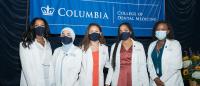 Five women from the Class of 2025 standing together wearing their white coats and face masks